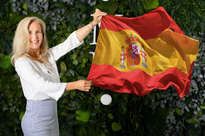 MoosMoos Vertriebmitarbeiterin Aglaja Albers aus Spanien steht einer vor Dschungel Mooswand und hält die spansicher Flagge